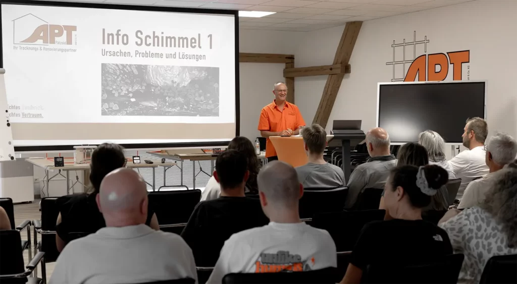 Referent in orangem Hemd hält Vortrag über Schimmel vor Publikum im APT Pätzold Schulungsraum